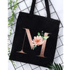 Black canvas tote bag featuring a large gold letter M with pink floral accents