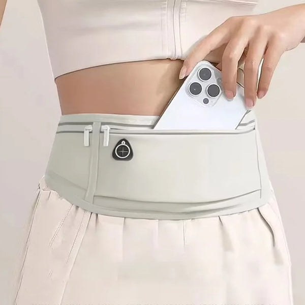 A woman wearing a light pink top and white shorts is holding a white multi-use waist pack with a phone attached.