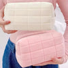 A person holds two quilted cosmetic storage pouches, one white and one pink.