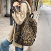 A woman wearing a beige jacket and jeans is carrying a leopard print canvas backpack while walking on a sidewalk.