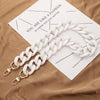 A white acrylic handbag strap chain is laid across a brown paper with black text.