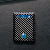 A black wallet with a carbon fiber texture and a blue RFID-blocking front pocket visible on a dark surface.