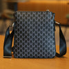 A black men's lightweight crossbody sling bag with a textured monogram pattern resting on a wooden surface.