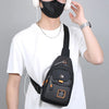 A person wearing a black face mask and headphones holds a black Oxford crossbody sling bag against a white t-shirt.