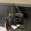 Bolso cruz de cuero suave negro de lujo con herrajes plateados sobre una superficie oscura.
