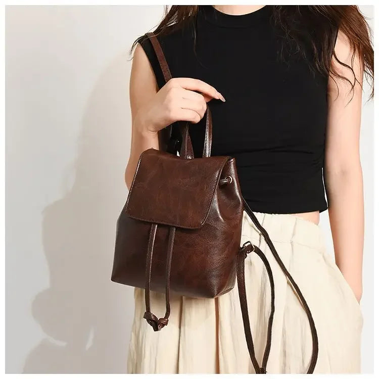 Une femme portant un haut noir et un pantalon clair tient un mini sac à dos en cuir marron à cordon.