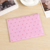 A pink heart print passport cover travel wallet resting on a light wooden surface.