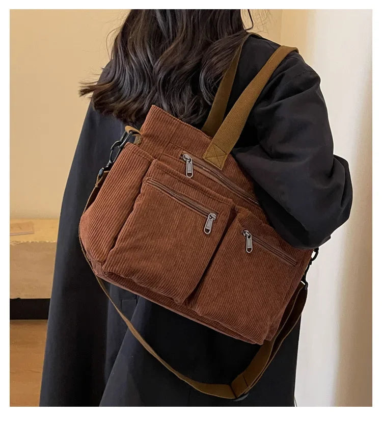 A person is carrying a brown textured corduroy tote bag with adjustable straps over their shoulder.