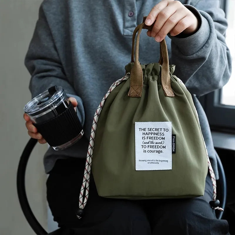 A person holds a olive green waterproof insulated lunch bag with brown drawstrings.