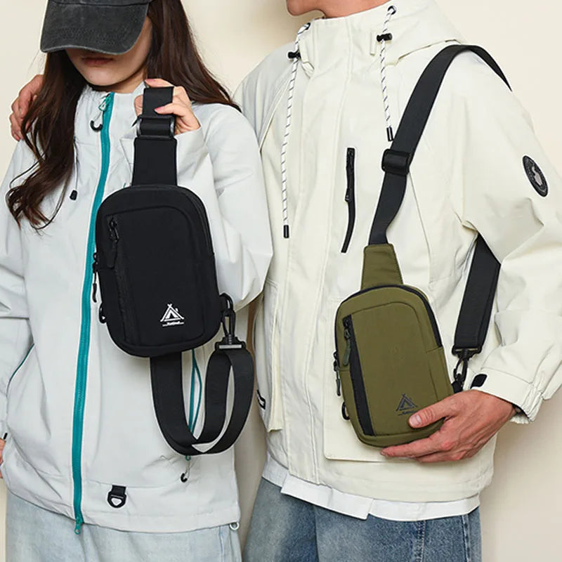 A person is holding a beige nylon sling crossbody bag with a dark green strap and pocket on their white jacket.