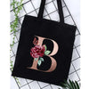 Black canvas tote bag featuring a large gold letter B with floral accents