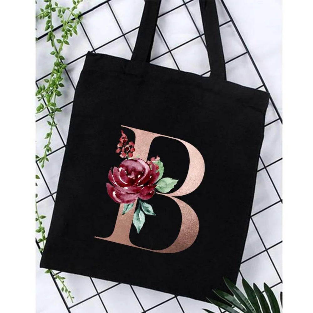 Black canvas tote bag featuring a large gold letter B with floral accents