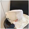 A white PU leather crossbody saddle bag with a chain strap resting on a black leather surface.