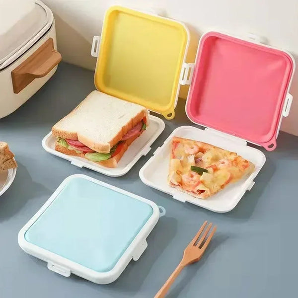 A collection of silicone reusable sandwich and lunch containers in yellow, pink, and light blue are displayed on a gray surfa