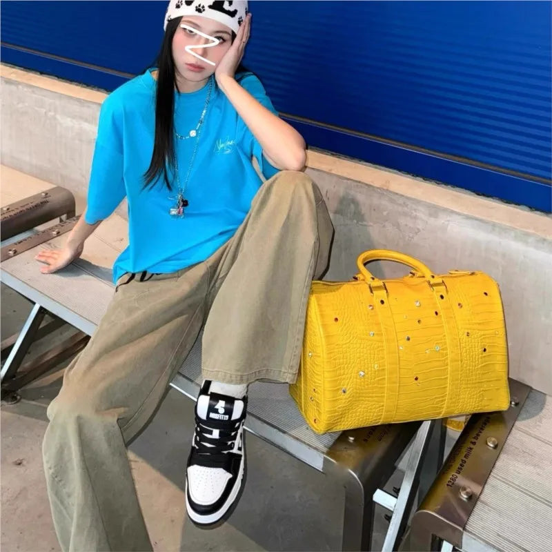 A woman wearing a blue shirt and tan pants poses with a yellow faux crocodile tote bag.