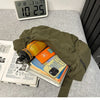 A olive green cotton canvas shoulder crossbody bag is shown open on a gray surface next to a digital clock and some papers.