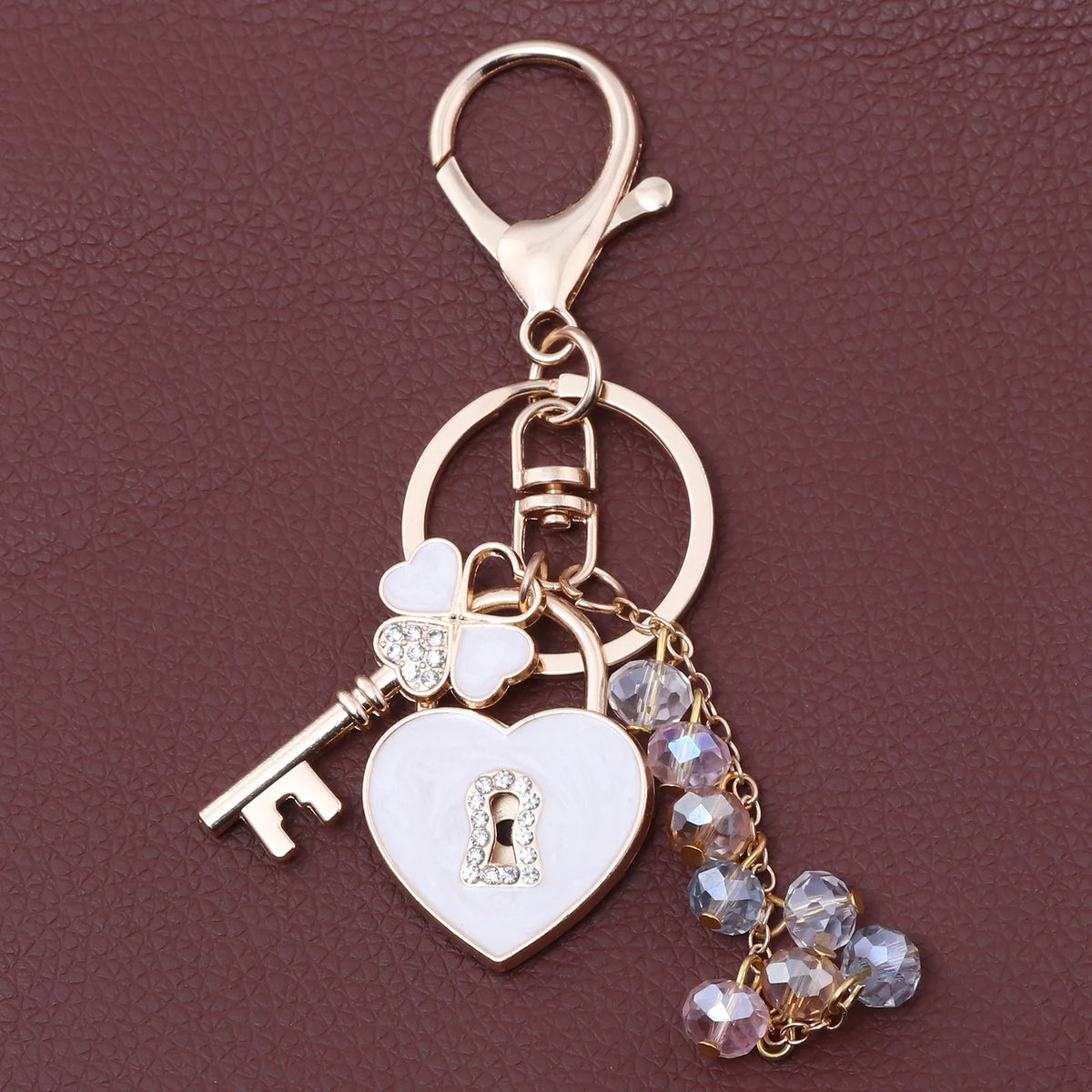 Gold-toned key chain featuring a heart and a flower charm with clear rhinestones
