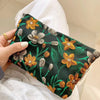 A dark green cosmetic pouch featuring a floral pattern of yellow and gray flowers being held by a hand.
