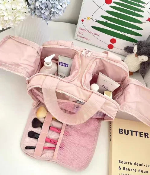 A pink multipocket travel toiletry bag with a mesh pocket and a lid is shown next to a skincare product.