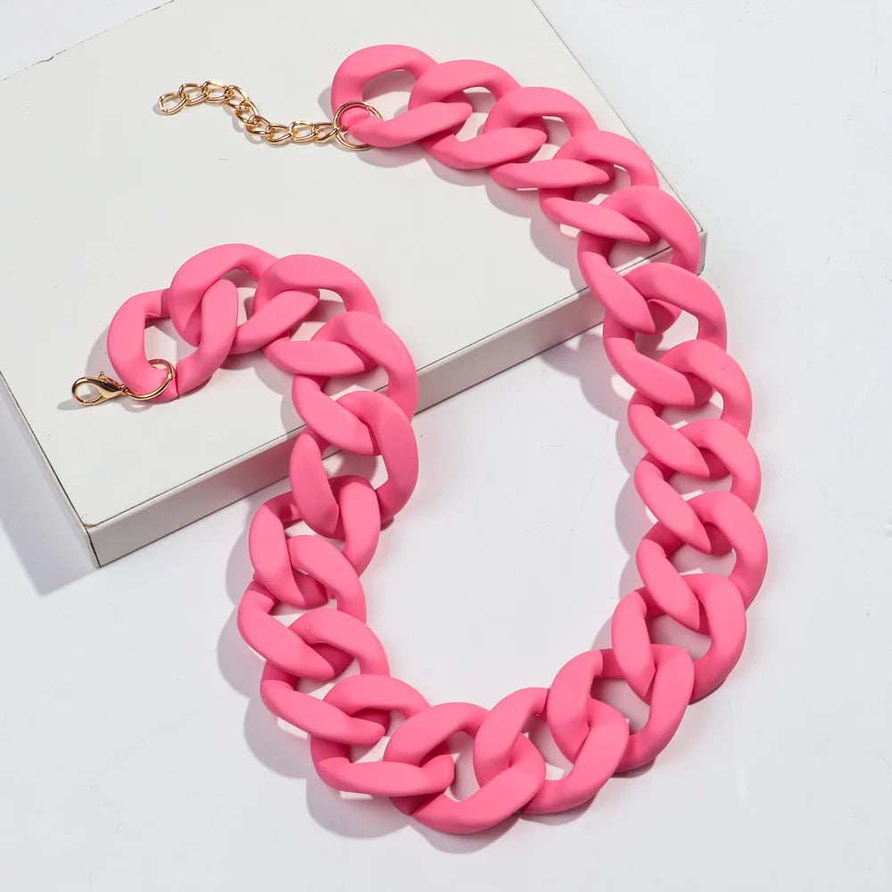 A pink matte acrylic chain necklace with a gold-colored clasp is displayed on a white box.