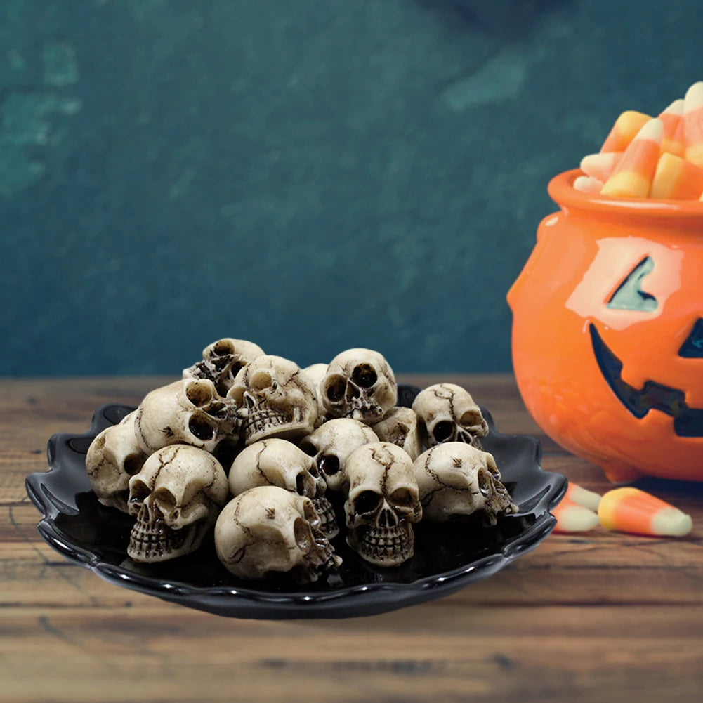 Una pila de esculturas de cráneos de resina realistas en un plato negro con dulces de Halloween de fondo.