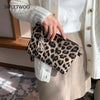 A hand holds a leopard print PU leather wrist bag against a white knit sweater and beige skirt.