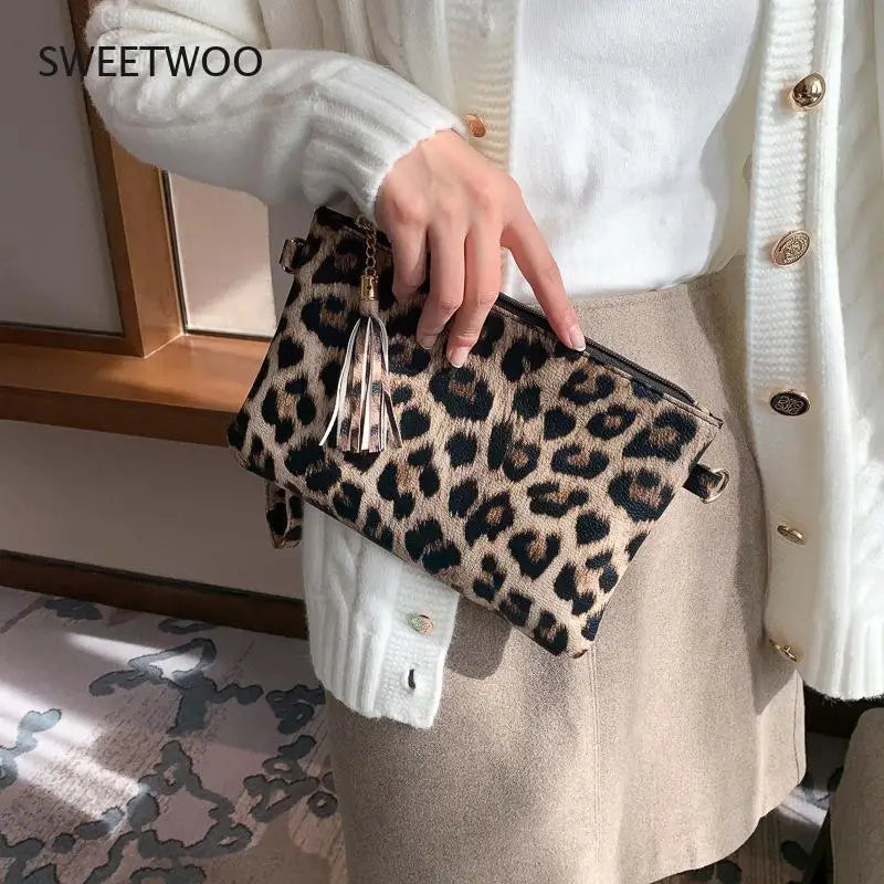 A hand holds a leopard print PU leather wrist bag against a white knit sweater and beige skirt.