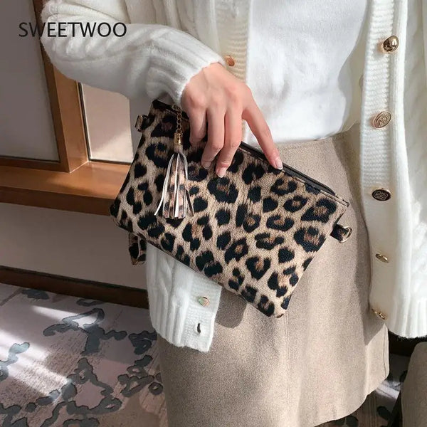 A hand holds a leopard print PU leather wrist bag against a white knit sweater and beige skirt.
