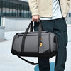 A person is holding a large capacity travel duffel bag in black and gray against a light background.