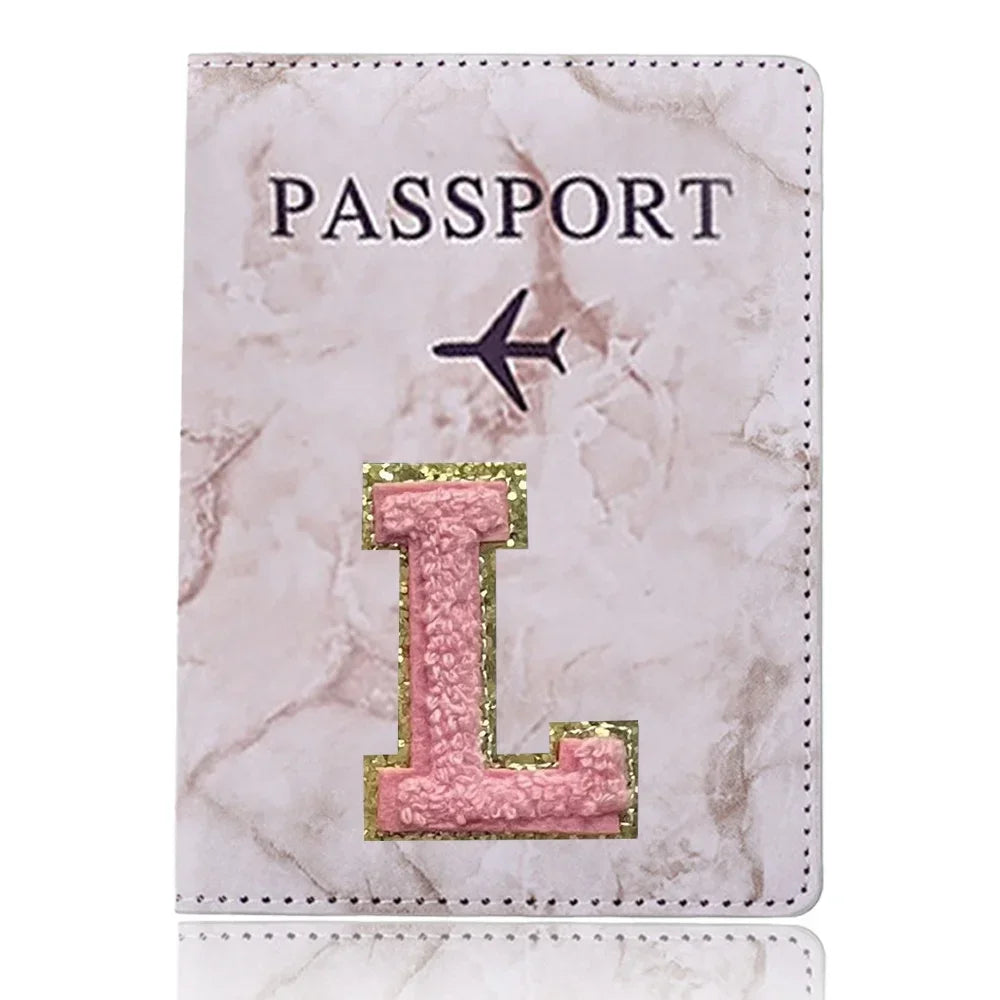 Carátula de pasaporte de cuero marmolado rosa con una inicial L dorada e ícono de avión negro.