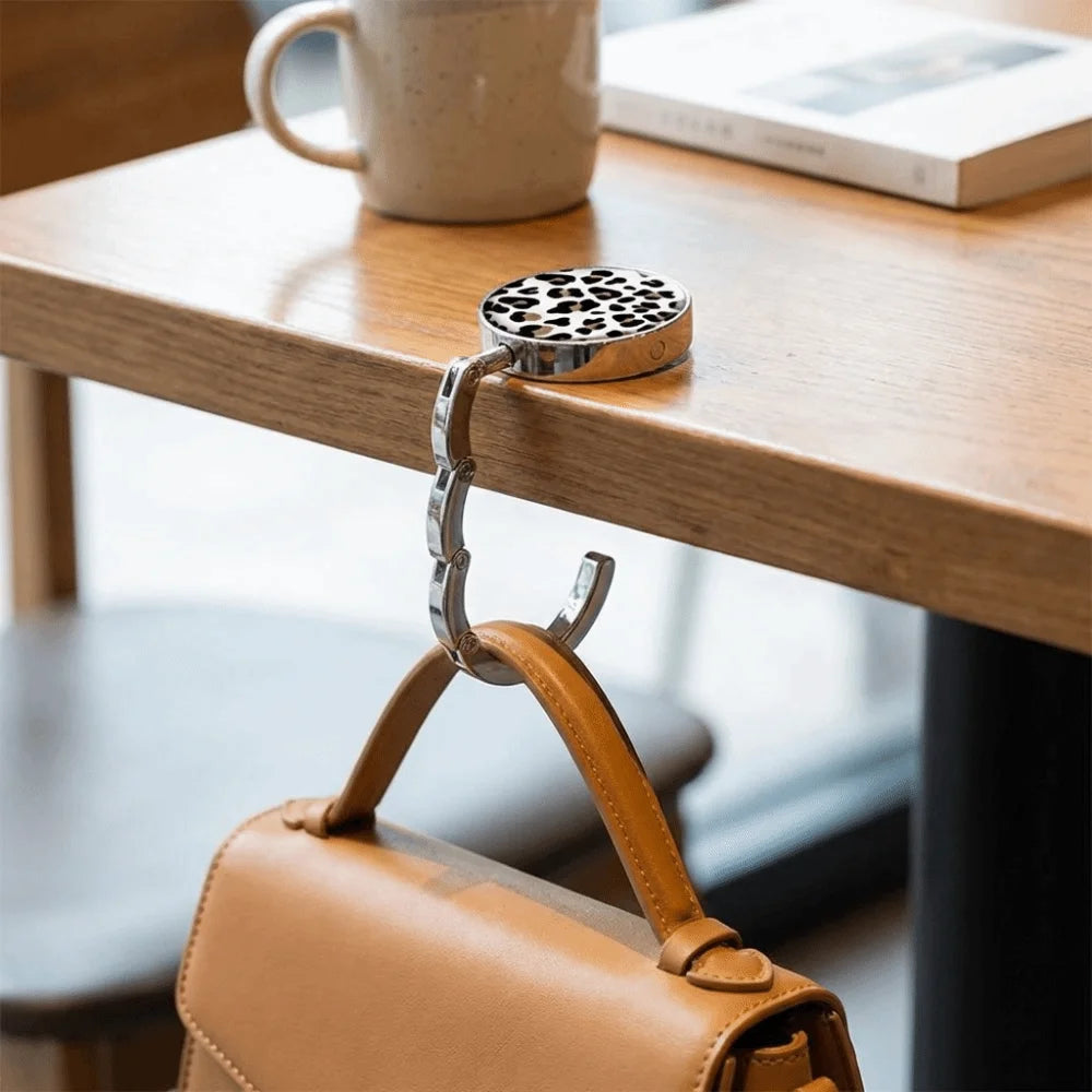 A round metal bag hanger with a leather strap is resting on a wooden table.