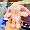 A pink plush rabbit toy with pink ears and a white tag is held in a person's hand.