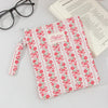 A pink and white floral plaid cotton tablet pouch with a ribbon closure resting on a piece of paper.