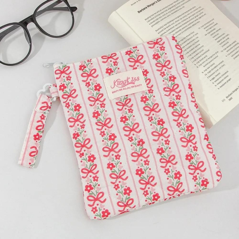 A pink and white floral plaid cotton tablet pouch with a ribbon closure resting on a piece of paper.