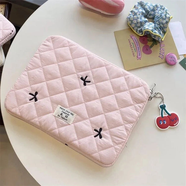 Housse de protection rembourrée rose et fine pour MacBook ou tablette, posée sur une table blanche.