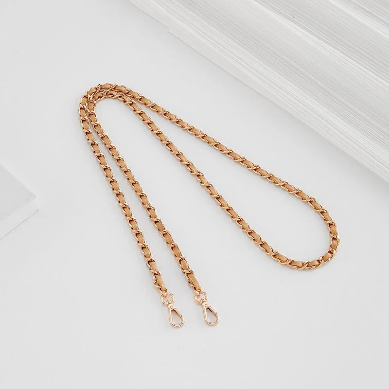 A close-up of a gold-toned braided leather strap with adjustable buckles lying on a white surface.