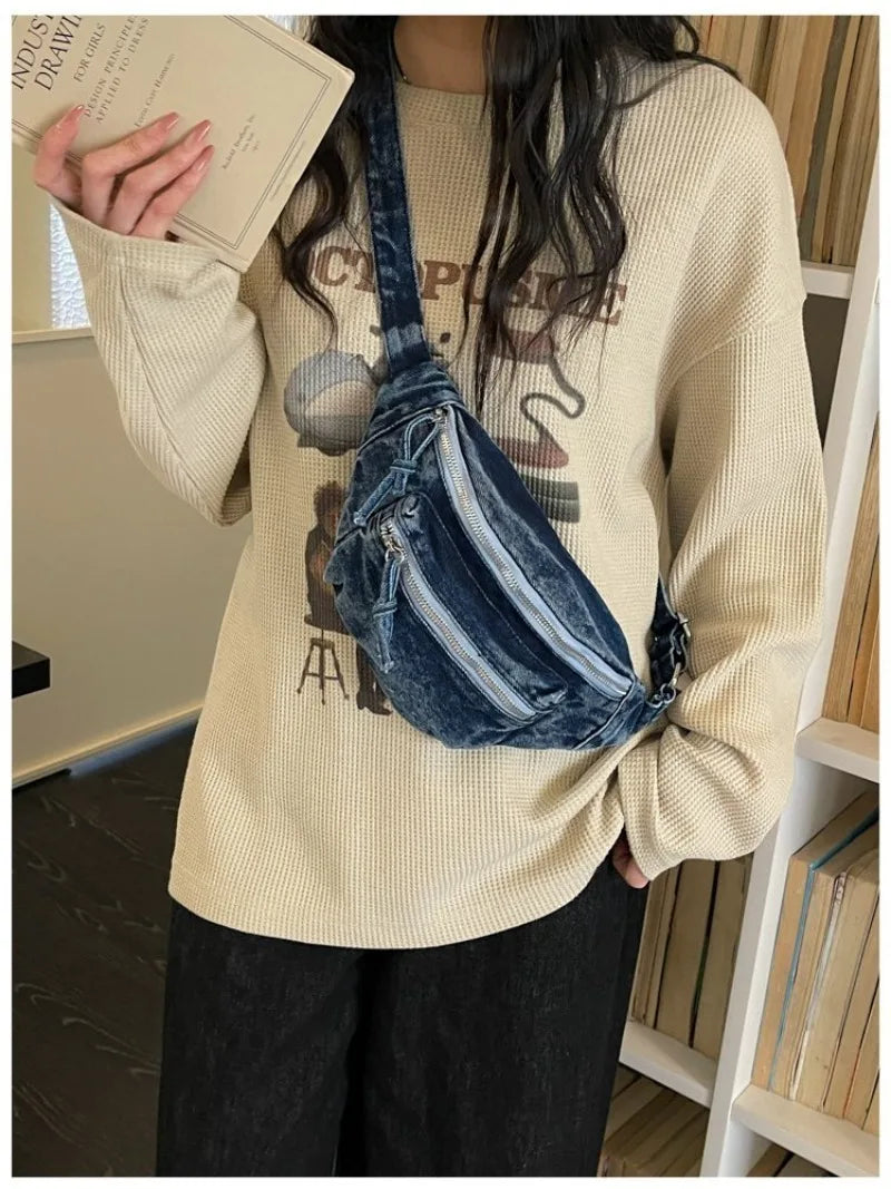 Une femme portant un pull crème et un pantalon foncé tient un sac bandoulière en denim vintage délavé.