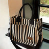 Sac bandoulière en toile rayée tendance avec bretelles noires, exposé dans un cadre de vitrine.