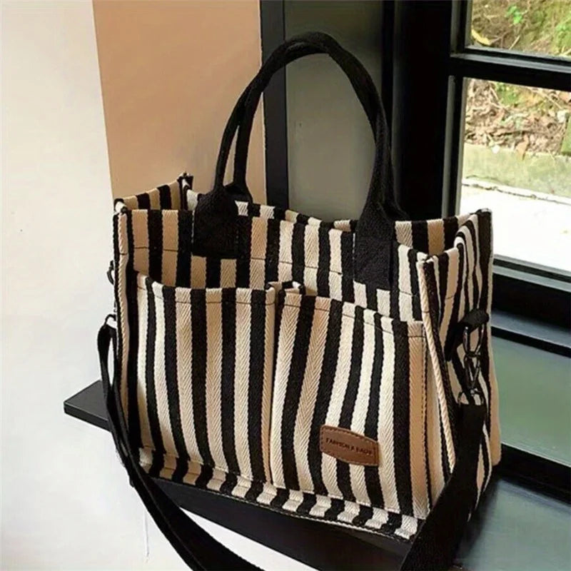 Sac bandoulière en toile rayée tendance avec bretelles noires, exposé dans un cadre de vitrine.