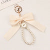 Llavero decorativo dorado delicado con dije de corbata y una hilera de perlas pequeñas.