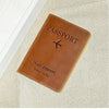 A brown genuine leather passport holder with stitching and a leather strap resting on a beige fabric background.