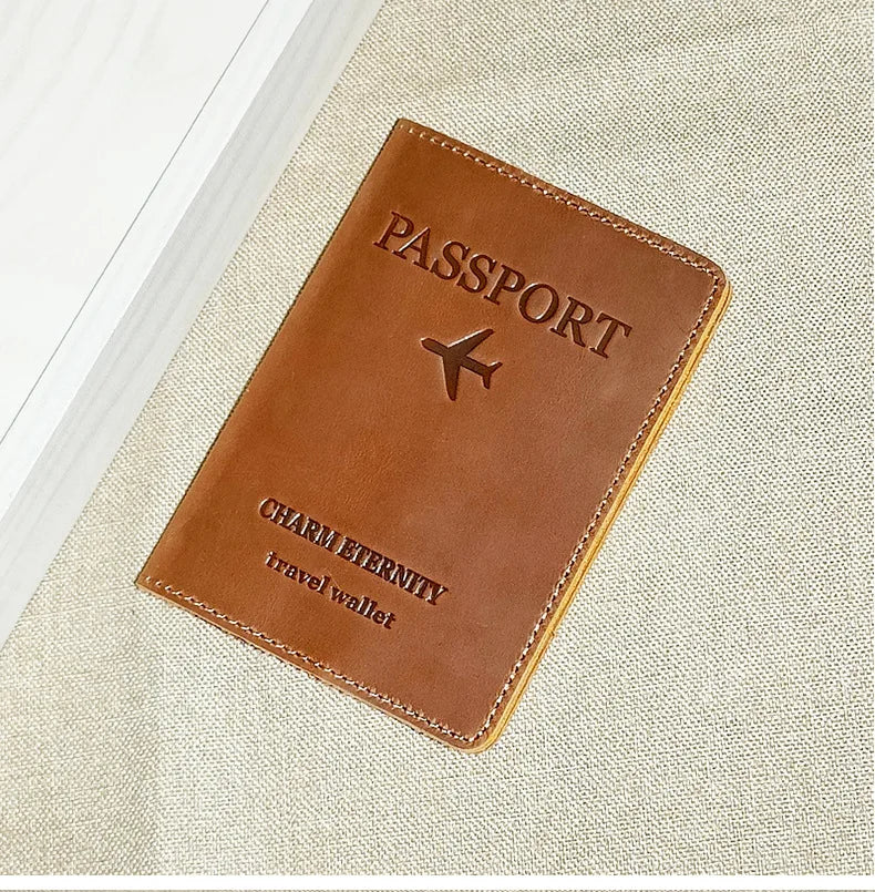 A brown genuine leather passport holder with stitching and a leather strap resting on a beige fabric background.