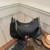 A black leather crescent crossbody bag with a gold chain strap is held against a white background.