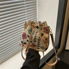 A close-up of a floral drawstring bucket bag in beige and pink tones being held by a person.