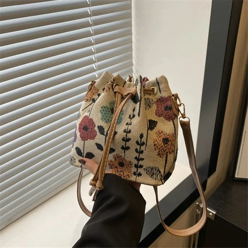 A close-up of a floral drawstring bucket bag in beige and pink tones being held by a person.