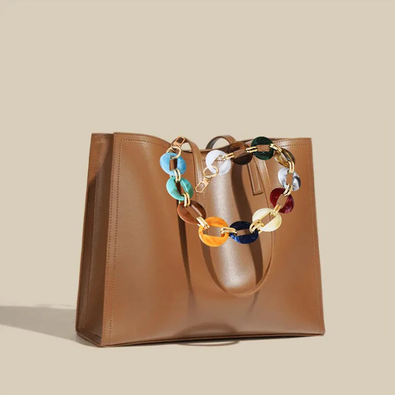 A tan leather handbag with a multi-color acrylic chain strap resting on a light beige background.