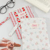 Two floral plaid cotton tablet pouches, one red and white, and one white with pink flowers, are displayed on a white surface.