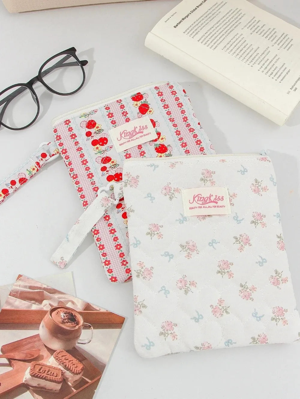 Two floral plaid cotton tablet pouches, one red and white, and one white with pink flowers, are displayed on a white surface.