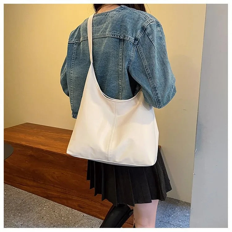 Ein weißer Canvas-Taschenbeutel wird von einer Person in einer Jeansjacke und einem schwarzen Rock getragen.