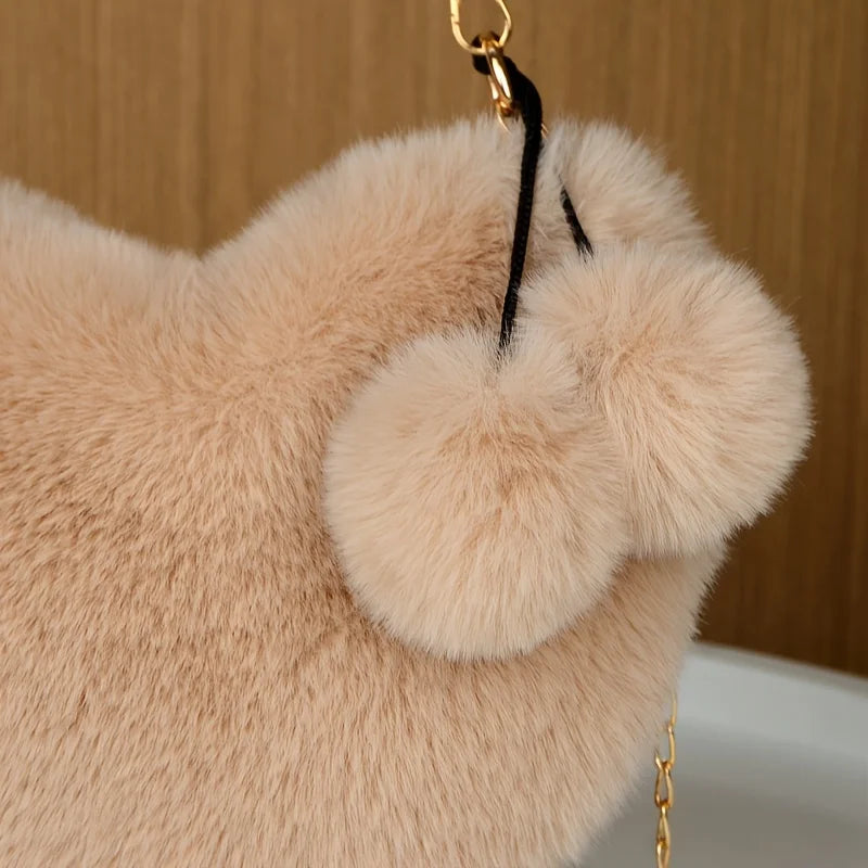 A light beige faux fur heart shaped crossbody purse with a black strap and gold hardware.
